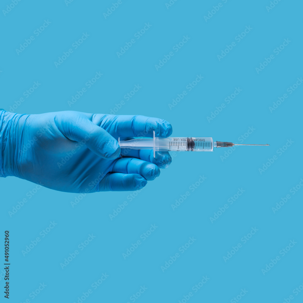 a hand in a blue medical glove with a syringe on a blue background a hand in a blue medical glove with a syringe on a blue background