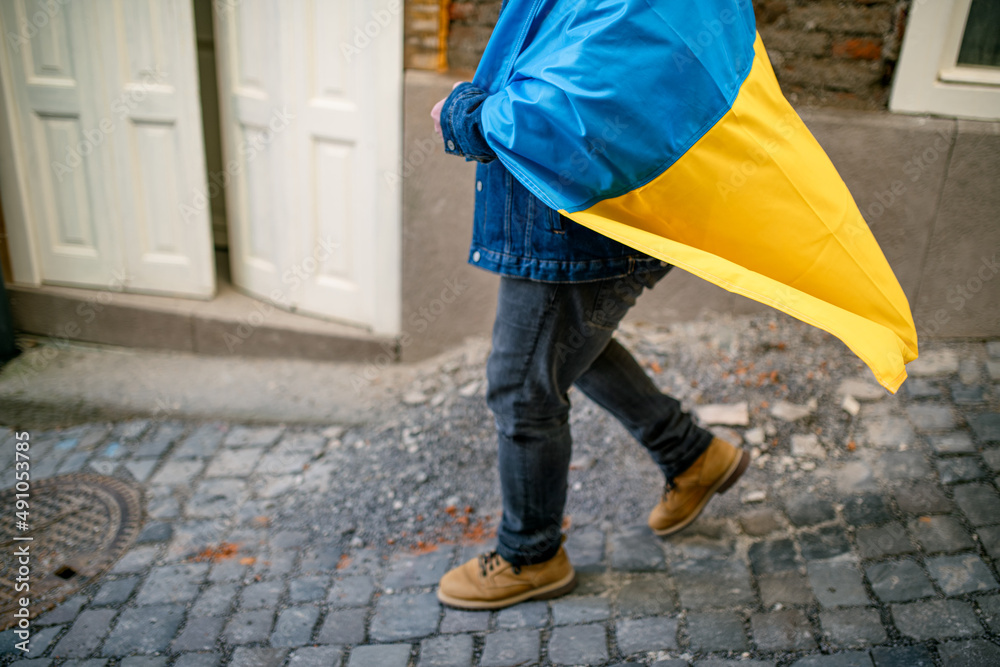 Lowsection of protestor covered with blue and yellow Ukrainian flag protesting against war in Ukraine in street