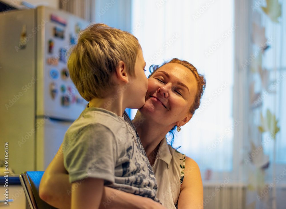 Obraz premium Cute little little baby, son hugging mom, hugging mom in the kitchen. Spend an evening with your family.