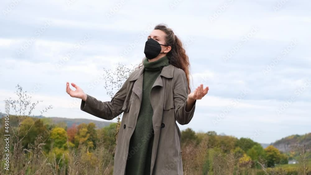Portrait of a beautiful, stylish hipster woman standing in autumn nature and putting on a black ffp2 respirator mask. Meeting with other people, self protection, social responsibility, covid concept. Portrait of a beautiful, stylish hipster woman standing in autumn nature and putting on a black ffp2 respirator mask. Meeting with other people, self protection, social responsibility, covid concept.