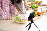 Selective focus at kitchen utensil and vegetable while people learn to cook by watch meal cooking tutorial or live video broadcast from smartphone. Unidentified people lifestyle.