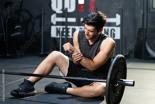 Фотография Young Caucasian men grab his arm and wrist and feeling painful while weight lifting exercise inside of sport gym