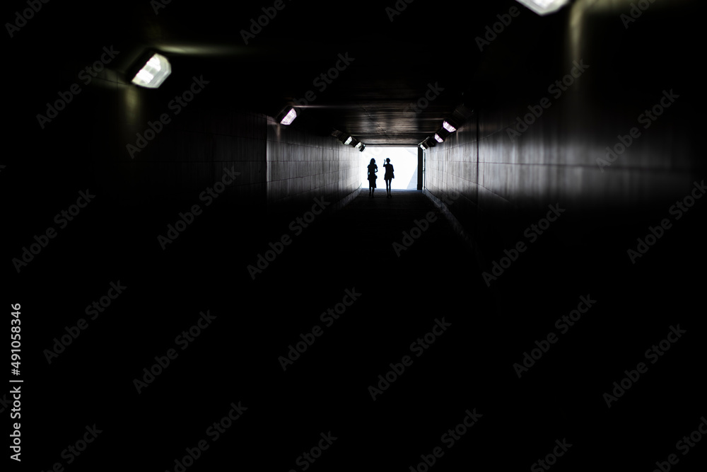 Two silhouettes at end of tunnel. Light in distance. Figures of small women in contrasting light.