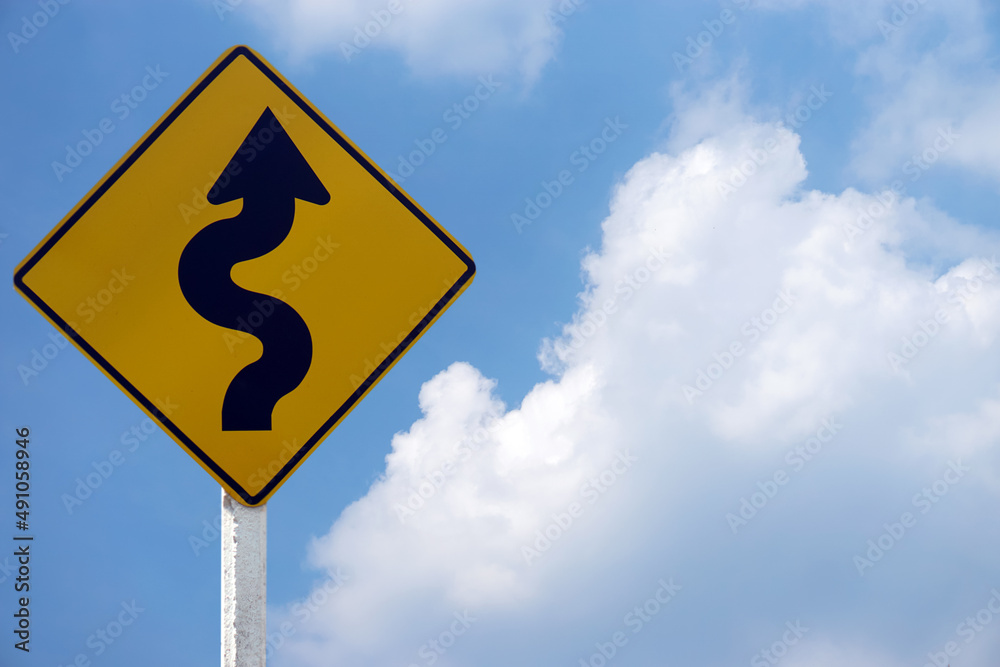 Yellow traffic sign with twisty arrow symbol to warn drivers be careful when driving on twisty way road. Concept : Warning traffic sign for transportation. Blue sky scene. Yellow traffic sign with twisty arrow symbol to warn drivers be careful when driving on twisty way road. Concept : Warning traffic sign for transportation. Blue sky scene.