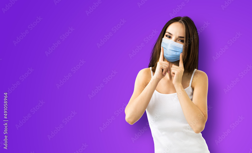 Coronavirus, covid-19, pandemic, protective concept - brunette happy smiling woman wearing showing face protection medical mask, violet purple background. Copy space area for some sign text.