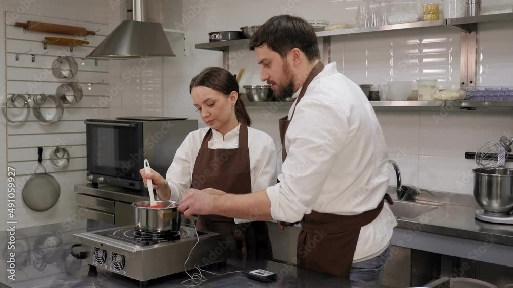 Two confectioners prepare mousse cake in a professional kitchen, measure the temperature of pistachio mousse with a kitchen thermometer. Two confectioners prepare mousse cake in a professional kitchen, measure the temperature of pistachio mousse with a kitchen thermometer.