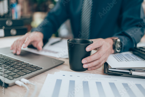 Accountant hold cup of coffee and working on company data, document and report on desk office. Accounting business concept.