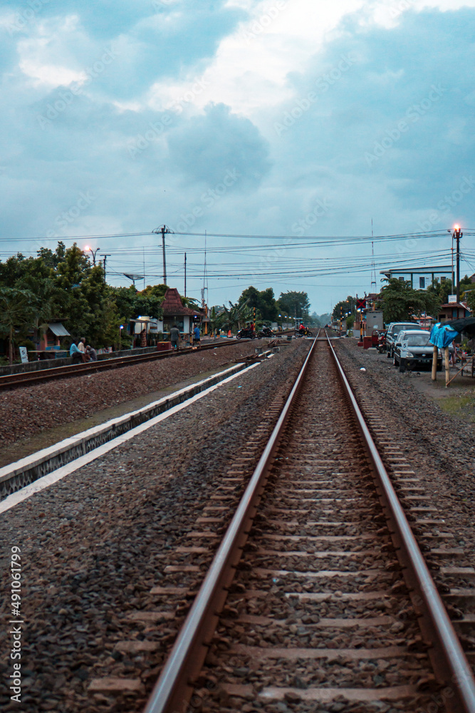 Obraz premium A railroad track made of iron, wood and gravel in a suburban area on a cloudy day in Indonesia