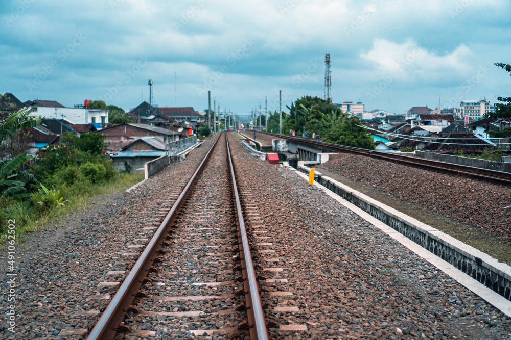  A railroad track made of iron, wood and gravel in a suburban area on a cloudy day in Indonesia