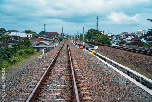  A railroad track made of iron, wood and gravel in a suburban area on a cloudy day in Indonesia