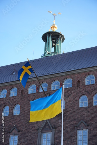 Stockholm, Sweden - March 05, 2022. Ukraine and Sweden flag on pole waving in wind. Swedish and ukrainian symbol in front of City hall world peace nobel prize stadshuset photo