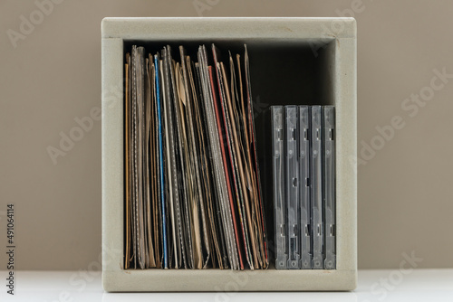 7 inch vinyl records and cd's in a wooden storage cube, set on a white shelf with brown background.