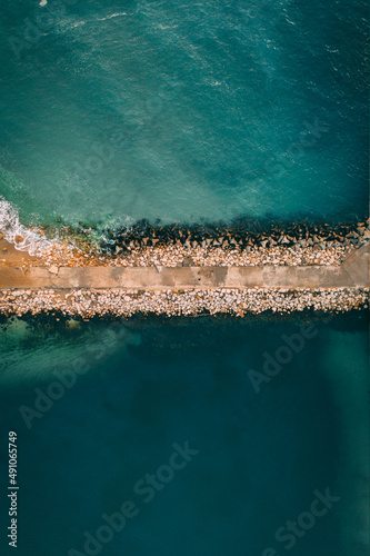 Top down drone shot of a rocky highway in the middle of the ocean at sunrise.