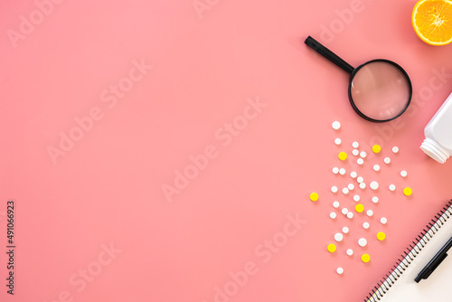 Flat lay, pills and magnifier on pink background, copy space.