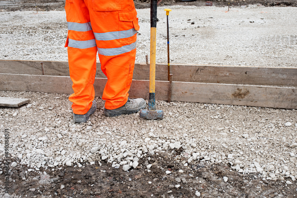 Groundworker making shutter for concrete to form a base for kerb using scaffold boards and steel road pins during new road construction Groundworker making shutter for concrete to form a base for kerb using scaffold boards and steel road pins during new road construction
