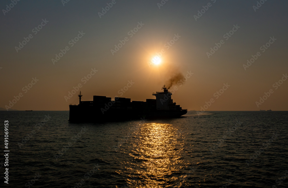 Silhouette Container ship sailing in middle of the sea and over the sunset background at evening