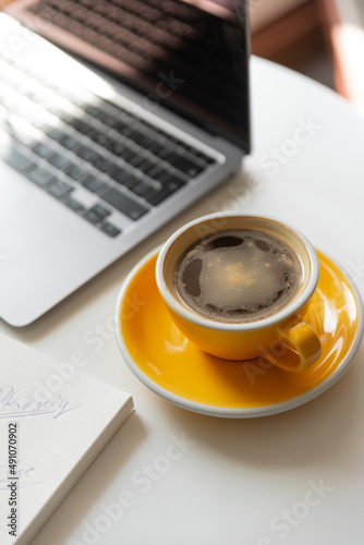 Yellow cup of coffee on workspace on table near laptop. 
