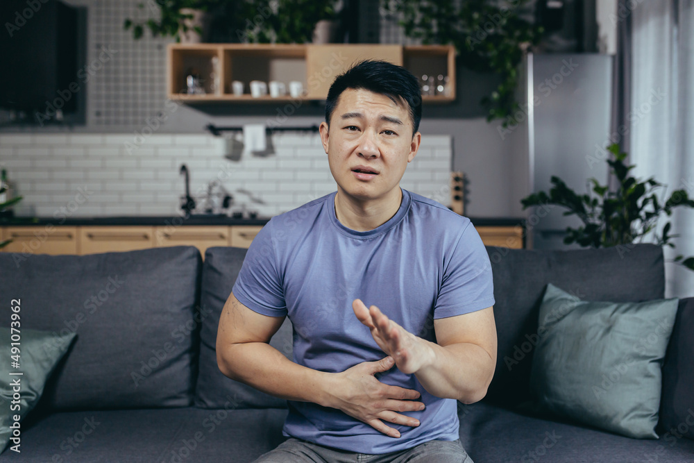 a man calls a doctor on an online video call, an Asian patient at home, points to abdominal pain a man calls a doctor on an online video call, an Asian patient at home, points to abdominal pain