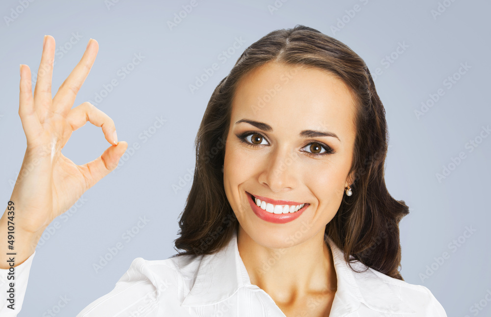 Businesswoman in white confident clothing showing ok hand sign gesture, isolated over gray background. Portrait of happy smiling gesturing brunette woman at studio. Business concept photo. Businesswoman in white confident clothing showing ok hand sign gesture, isolated over gray background. Portrait of happy smiling gesturing brunette woman at studio. Business concept photo.