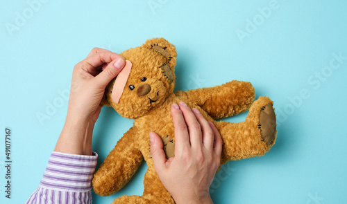female hand holds a brown teddy bear and glues a medical adhesive plaster on a blue background, tram treatment photo