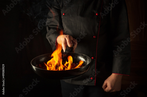Professional chef cooking food in pan with fire flame on black background. Restaurant and hotel service concept. European cuisine. Vegetarian cuisine.