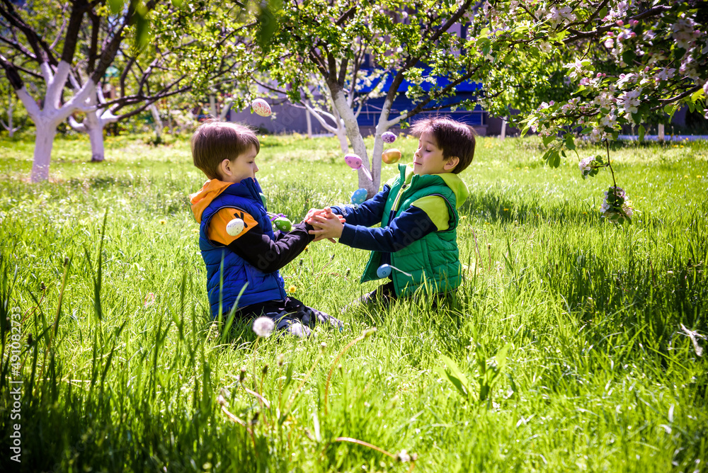 Fototapeta premium Kids on Easter egg hunt in blooming spring garden. Children searching for colorful eggs in flower meadow. Toddler boy and his brother friend kid boy play outdoors