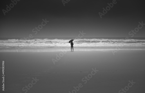 silhouette mit regenschirm am strand mit hohen wellen, sportlich kalt am sandstrand dunkler hintergrund