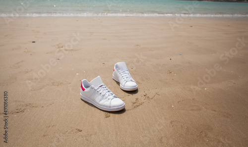 a pair of summer white shoes standing on the sand on the ocean shore