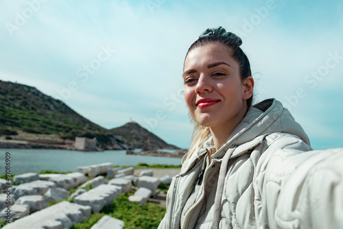 Happy beautiful woman takes a selfie portrait on vacation outdoor. She is in archaeological site. Travel alone concept.