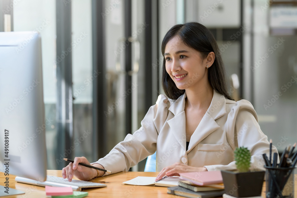 Beautiful young Asian businesswoman is smiling at her desk and taking notes with computer laptop on her desk, enjoying work. Beautiful young Asian businesswoman is smiling at her desk and taking notes with computer laptop on her desk, enjoying work.