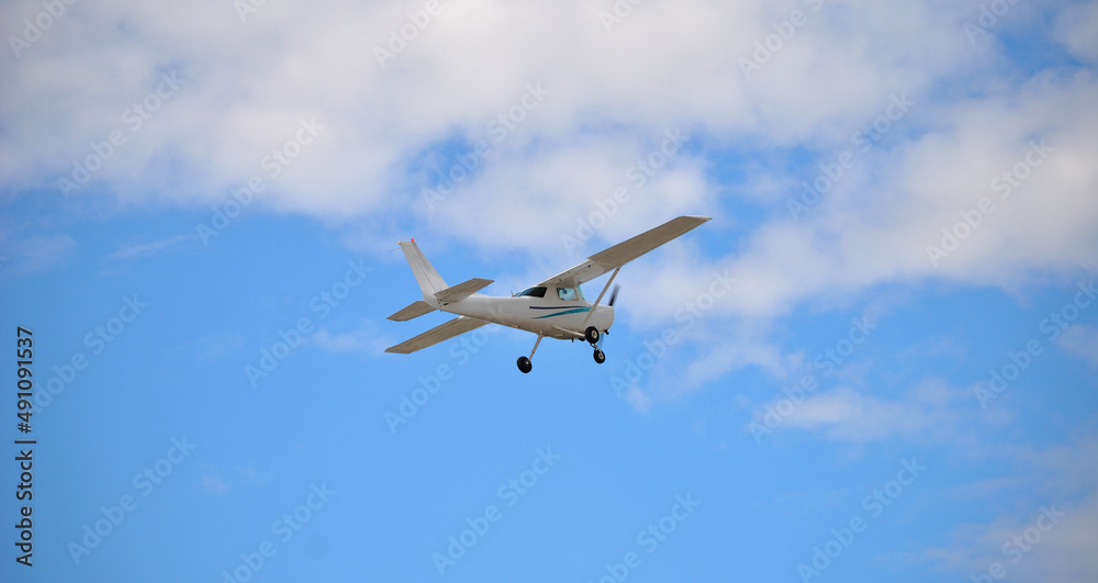 Pequena avioneta branca a levantar voo, vista por baixo de e trás, céu azul com nuvens brancas