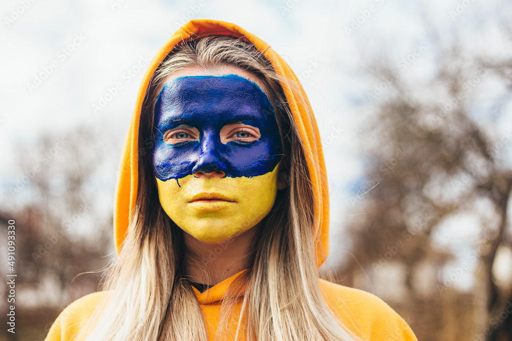 Outdoor portrait of young girl with blue and yellow ukrainian flag on her face Outdoor portrait of young girl with blue and yellow ukrainian flag on her face