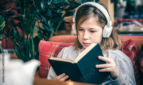 A little girl reads a book and listens to music on headphones.
