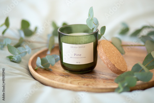 Foto Green scented candle and a branch of eucalyptus on a wooden tray.