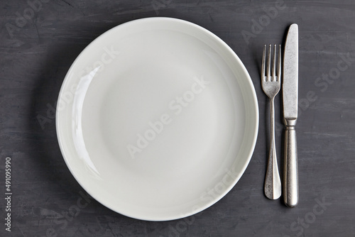 White plate on a dark concrete background with cutlery
