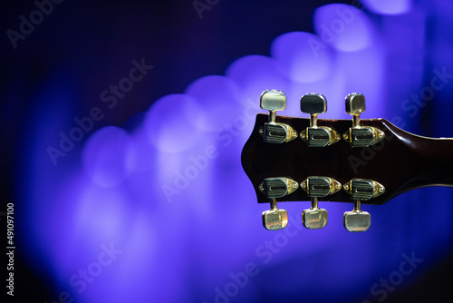 The headstock and neck of an electric guitar against the lights during a concert.