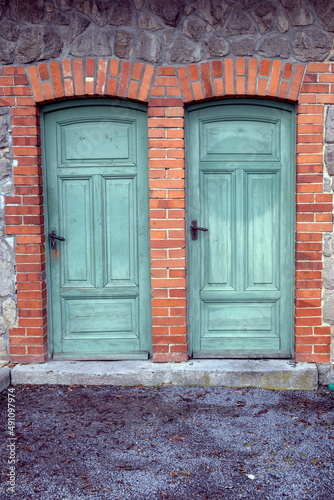 two old green wooden doors at building with brick wall
