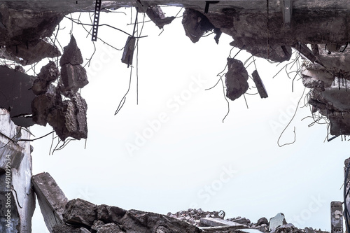 A hole in the body of a building with a pile of construction debris and concrete fragments hanging on the rebar against a uniform gray sky. Background © Roman