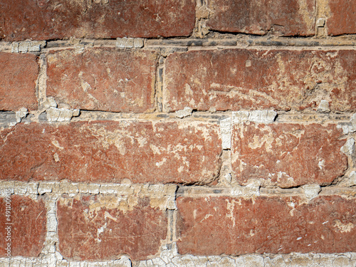 Fragment of old brickwork. Flat lay, close-up. Cracks and defects in the red brick on the wall are illuminated by bright light. Potholes and defects in red brick.