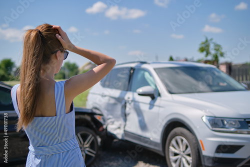 Sad young woman driver standing near her smashed car looking shocked on crashed vehicles in road accident © bilanol
