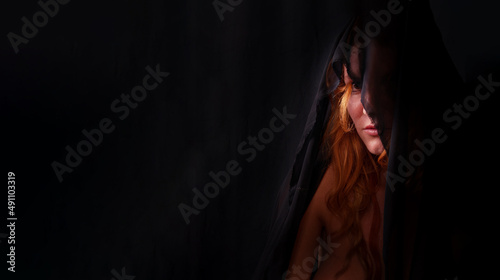 portrait of a beautiful seductive sensual, young, sexy redhead woman, hides shyly behind black cloth, one eye looks out shy