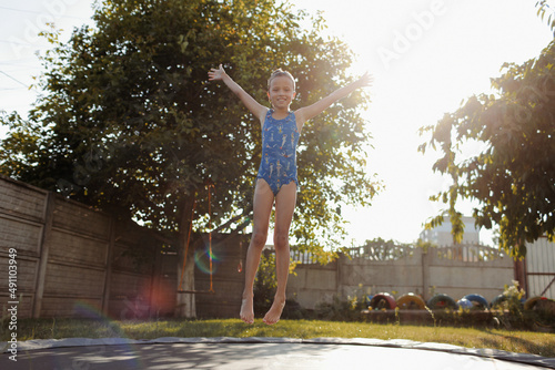 little sports girl jumps on a trampoline. Outdoor shot of girl jumping on trampoline, enjoys jumping in home. happy summer vacation