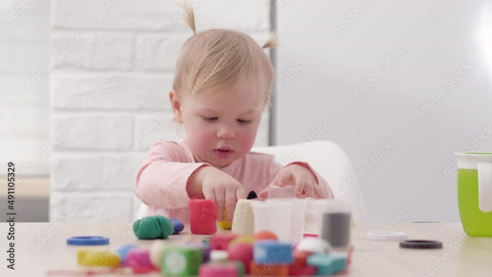 Cute Little girl with funny ponytails on head sitting in kitchen and playing multicolored plasticine, 2 years Kid girl having fun with modeling clay at home, Early education and development Cute Little girl with funny ponytails on head sitting in kitchen and playing multicolored plasticine, 2 years Kid girl having fun with modeling clay at home, Early education and development