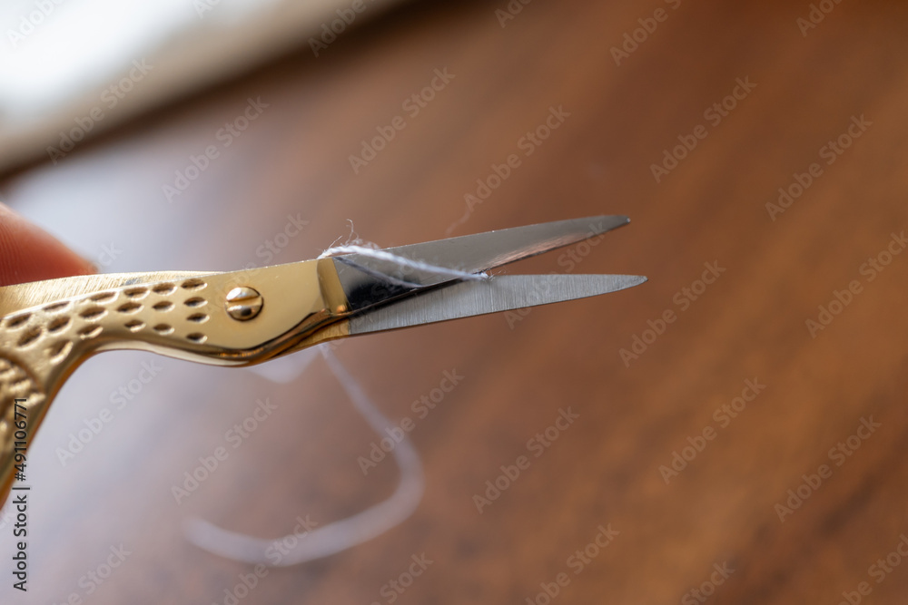 Obraz premium detalle de tijera para bordado a punto de cortar hilo gris sobre mesa de madera