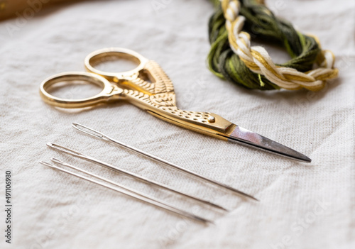 materiales para bordar, madejas de hilo de algodón verde y amarillo trenzados con aro de madera, tela manta, tijeras y agujas a la luz natural de la ventana photo