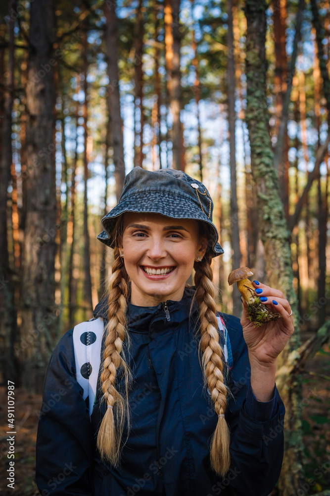 Young happy woman in black hat showing mushroom in pine forest Young happy woman in black hat showing mushroom in pine forest
