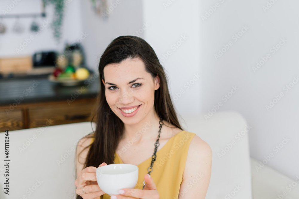 Cozy living room happy woman sitting on couch. European female enjoy lazy weekend or vacation Cozy living room happy woman sitting on couch. European female enjoy lazy weekend or vacation