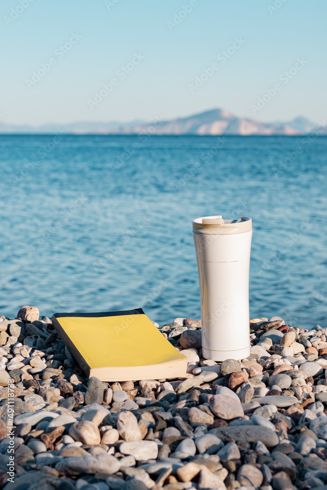 Coffee thermos and yellow book seaside. Gravel coast. Sun, sea, beach, reading and resting. Coffee thermos and yellow book seaside. Gravel coast. Sun, sea, beach, reading and resting.