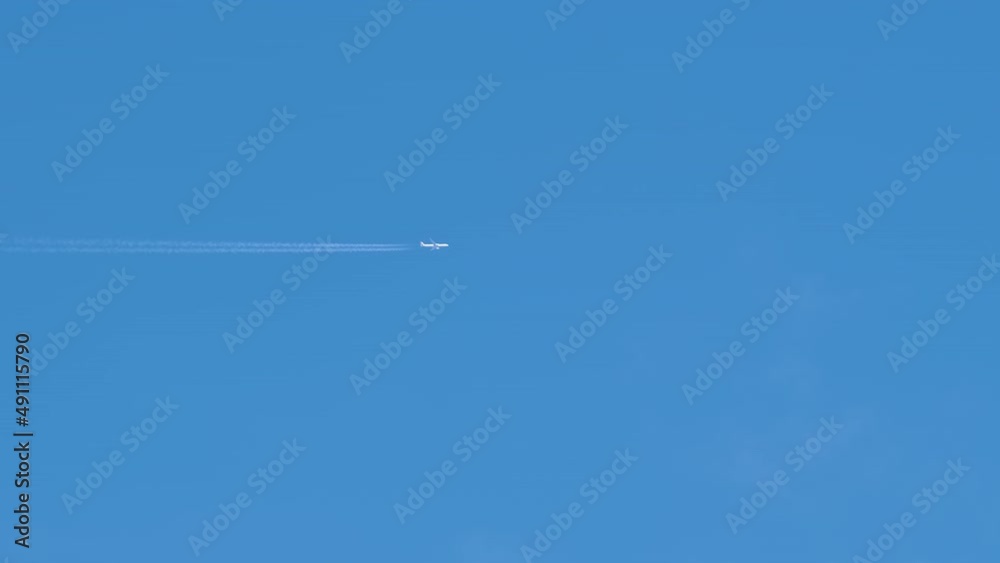 Distant passenger jet plane flying on high altitude on clear blue sky leaving white smoke trace of contrail behind. Air transportation concept Distant passenger jet plane flying on high altitude on clear blue sky leaving white smoke trace of contrail behind. Air transportation concept