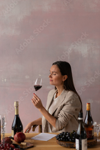 Beautiful female sommelier on degustation of wine on pink background photo